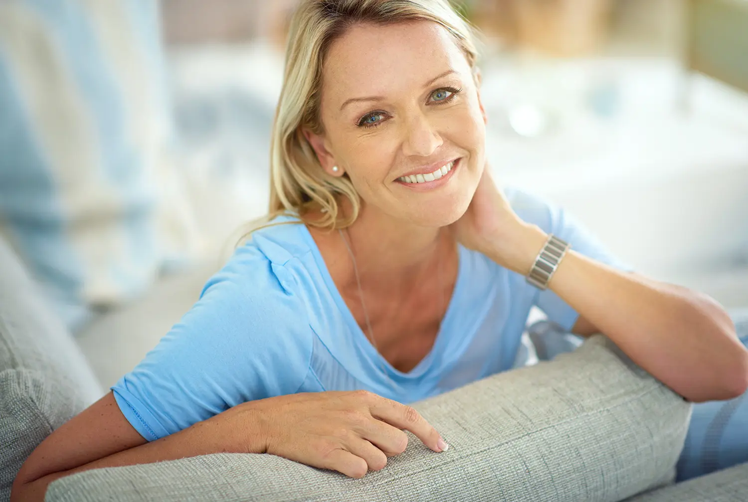 woman in blue shirt smiling and leaning on the couch